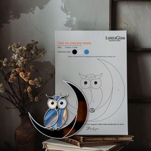 Peut inclure: Un hibou en vitrail perché sur un croissant de lune. Le hibou est en verre bleu et blanc, et la lune est marron. Le design mesure 18 cm x 18 cm. Un schéma et le texte "Owl on crescent moon" sont visibles.