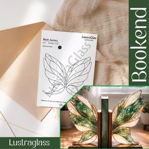 Könnte beinhalten: Buchstützen in Schmetterlingsform mit grünen und weißen Glasflügeln. Die Buchstützen sind aus Holz gefertigt und stehen auf einem Holzsockel. Ein Papier mit dem Text "Blush Aurora" und "Lustraglass" ist ebenfalls sichtbar.