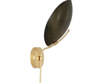 May include: A wall-mounted sconce with a brass finish. The sconce features a dark, oval-shaped shade and a slender, curved arm. The design is minimalist and elegant, suitable for interior lighting.