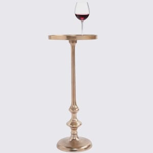 Puede incluir: Una mesa auxiliar decorativa de color dorado con una parte superior redonda y un tallo alto y delgado. Una copa de vino llena de vino tinto se encuentra sobre la superficie de la mesa. La mesa tiene una base decorativa y está diseñada para sostener bebidas.