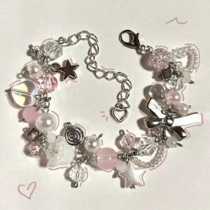 May include: A delicate bracelet featuring a mix of pink, white, and clear beads. The bracelet includes star and heart charms, along with silver-toned metal accents. The design incorporates pearls and various bead shapes.