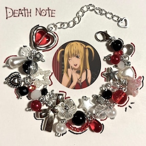 Puede incluir: Una pulsera de plata con un dije redondo de un personaje de anime. La pulsera incluye cuentas rojas, negras, blancas y transparentes, junto con dijes de corazón, estrella y cruz. Las palabras "Death Note" están escritas en tinta negra en la parte superior.