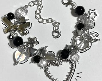 May include: A silver charm bracelet featuring a variety of charms, including a bow, hearts, stars, and beads. The bracelet incorporates black and clear beads, and a large openwork heart charm. The bracelet has a lobster clasp closure.