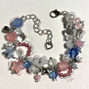 May include: A delicate charm bracelet featuring a variety of beads in pastel colors. The bracelet includes pink hearts, blue and clear flower-shaped beads, and pearl accents. The chain is silver-toned with a heart-shaped charm.