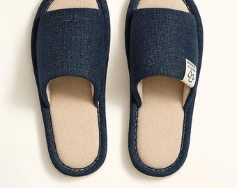 Könnte beinhalten: Ein Paar marineblaue Pantoletten mit offener Spitze, beigefarbenem Fußbett und weißen Nähten. Die Pantoletten haben ein Obermaterial aus strukturiertem Stoff und ein kleines Etikett. Das Wort "ONYRA" steht unten.