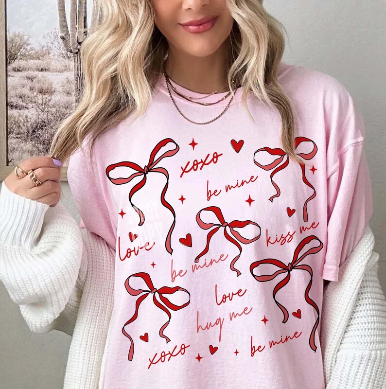 May include: Pink t-shirt with red ribbon graphics and romantic phrases like "Love," "Be Mine," and "Kiss Me." The design includes hearts and stars, creating a Valentine's Day or romantic theme.