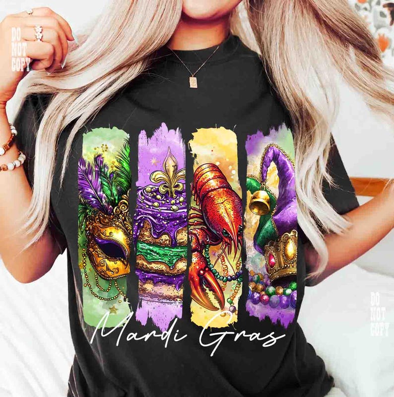 May include: Black t-shirt featuring a colorful Mardi Gras design. The design includes a gold mask with purple and green feathers, a slice of cake with a fleur-de-lis, a red crawfish, and a purple jester hat. The words "Mardi Gras" are written in white.