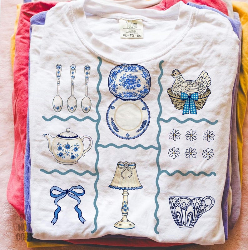 Pode incluir: Camiseta branca com um design floral azul e branco. O design inclui colheres, pratos, uma chaleira, uma galinha numa cesta, flores, uma l&acirc;mpada, um la&ccedil;o e uma ch&aacute;vena de ch&aacute;. A camisa tem uma etiqueta que diz "XL - TG - EG".