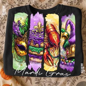 May include: Black sweatshirt featuring a colorful Mardi Gras design. The design includes a mask, cake, crawfish, and a jester's hat. The words "Mardi Gras" are written in white script across the bottom of the design.