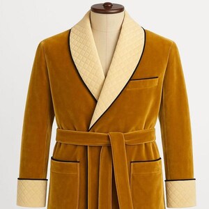 May include: Mustard yellow velvet robe with a quilted cream-colored collar and cuffs, trimmed with black piping. Features a matching belt and pockets. The robe is displayed on a mannequin.