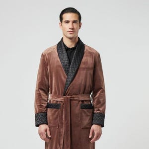 May include: A brown velvet robe featuring a black quilted shawl collar, black quilted cuffs, and two front pockets with black quilted trim. The robe includes a matching brown velvet tie belt at the waist and a black button-down shirt underneath.