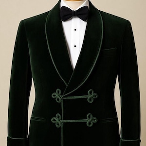 Puede incluir: Chaqueta de esmoquin de terciopelo verde oscuro con cuello chal y cierres de rana decorativos. La chaqueta presenta un diseño cruzado, una pajarita negra y una camisa blanca. Los puños y las solapas están ribeteados con un ribete verde contrastante.