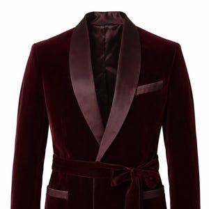 May include: A deep burgundy velvet blazer featuring a satin shawl collar, a matching waist tie with a bow, and satin-trimmed pockets. The jacket has long sleeves and a structured silhouette, crafted from a rich, dark red velvet fabric throughout.