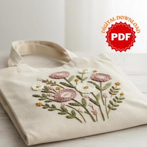 May include: Cream-colored tote bag with embroidered floral design. The embroidery features pink, white, and yellow flowers with green leaves. The bag has a handle and the text "DIGITAL DOWNLOAD PDF".