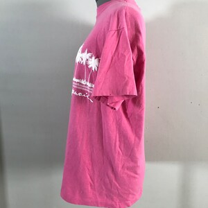 May include: Pink t-shirt with a white graphic of palm trees and the word "Hawaii" on the front.