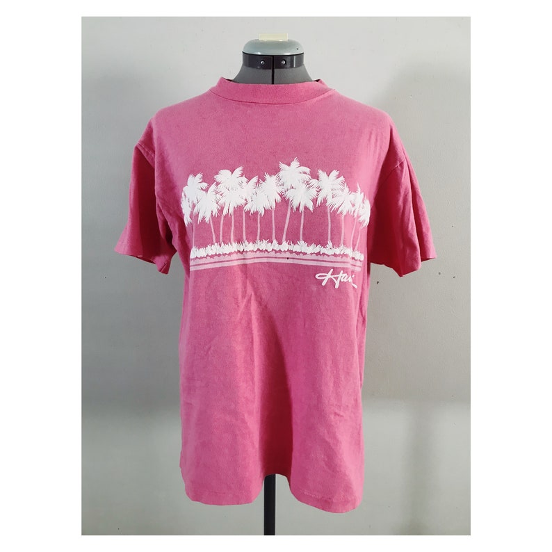 May include: A pink t-shirt with a white graphic of palm trees and the word "Hawaii" on the front.