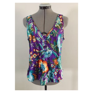 May include: A sleeveless purple top with a floral print in shades of orange, blue, and green. The top has a V-neck and a button closure at the center front.