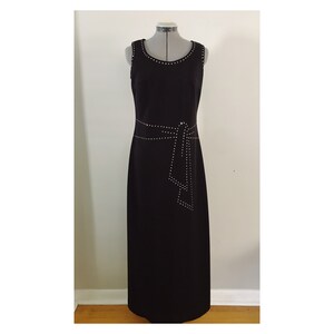 May include: A sleeveless black dress with a round neckline and a waist belt, both embellished with small, silver-colored studs. The dress is floor-length and displayed on a mannequin.