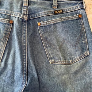 Puede incluir: Vaqueros de mezclilla azul con dise&ntilde;o de cintura alta, trabillas para cintur&oacute;n, canes&uacute; trasero y dos bolsillos traseros de parche. Cada bolsillo est&aacute; reforzado con remaches met&aacute;licos de color cobre y presenta una costura en forma de W. Etiqueta negra de Wrangler cosida.
