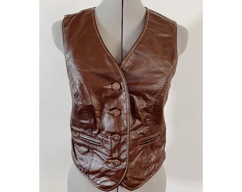 May include: A brown leather vest with a V-neck and four decorative buttons. The vest has two small pockets and is displayed on a mannequin. The vest is a vintage style.