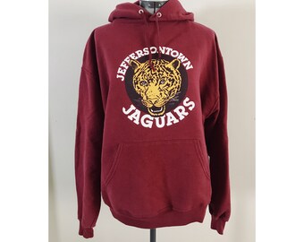 May include: Burgundy hooded sweatshirt with a white and yellow graphic of a jaguar's head in a circle with the text "Jeffersontown Jaguars".