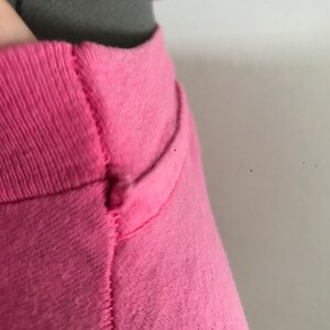 May include: Close-up of the neckline of a pink t-shirt. The shirt has a seam down the centre of the neckline.