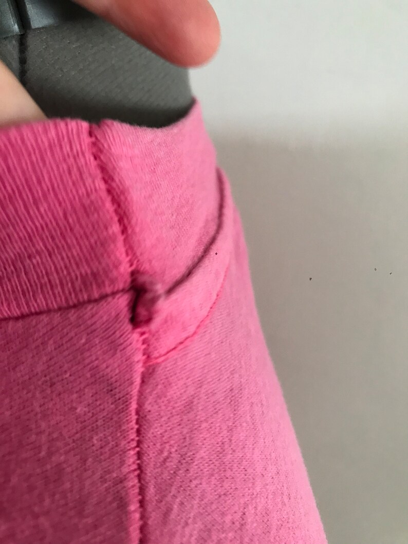 May include: Close-up of the neckline of a pink t-shirt. The shirt has a seam down the centre of the neckline.