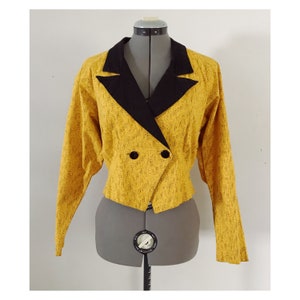 May include: A yellow blazer with a black collar and double breasted closure. The blazer has a textured pattern and is cropped.