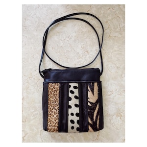 May include: Black leather crossbody bag with panels of animal print and black and white polka dots. The bag has a long, thin strap and a zippered top. The animal print includes leopard and zebra patterns.