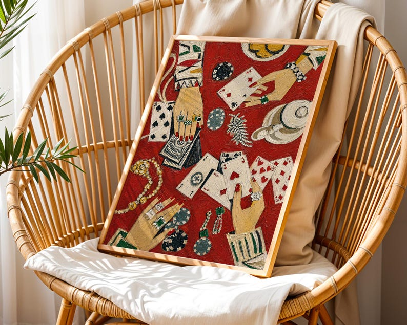 K&ouml;nnte beinhalten: Ein gerahmtes Kunstwerk mit rotem Hintergrund, das Spielkarten, mit Schmuck geschm&uuml;ckte H&auml;nde und Pokerchips zeigt. Das Kunstwerk wird auf einem Korbstuhl mit wei&szlig;em Kissen und beigem &Uuml;berwurf pr&auml;sentiert.