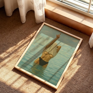 Puede incluir: Impresi&oacute;n art&iacute;stica enmarcada que representa a una persona en el agua, con una camiseta blanca y una parte inferior negra, con un brazo levantado en un gesto. La obra de arte est&aacute; enmarcada en un marco de madera clara, sobre una alfombra marr&oacute;n cerca de una ventana.