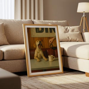 Puede incluir: Una impresi&oacute;n enmarcada que presenta a un perro bostezando en una mesa de restaurante mientras se vierte caf&eacute; en una taza. La impresi&oacute;n tiene un marco de madera clara y est&aacute; apoyada contra un sof&aacute; beige. El letrero del restaurante dice "DIN".