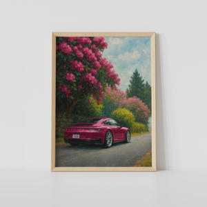 Könnte beinhalten: Gerahmter Kunstdruck eines roten Sportwagens auf einer Straße, gesäumt von rosa blühenden Bäumen und grünem Laub. Das Kunstwerk hat einen malerischen Stil, mit blauem Himmel und einer Steinmauer.