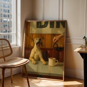Puede incluir: Una obra de arte enmarcada representa a un perro bostezando en una mesa de restaurante mientras se vierte caf&eacute; en una taza. La obra est&aacute; apoyada contra una pared junto a una ventana y una silla de madera. La escena est&aacute; ba&ntilde;ada por la luz natural.
