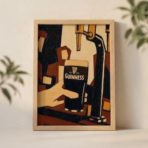 Op de afbeelding: Een ingelijste print met een Guinness pint die wordt geschonken. Het kunstwerk toont een hand die het glas vasthoudt, met het Guinness-logo. De achtergrond toont een barsc&egrave;ne met een biertap.
