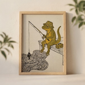 Puede incluir: Una impresión enmarcada que presenta una ilustración caprichosa de un lagarto pescando. El lagarto, con sombrero y collar, está sentado en un muelle de madera, sosteniendo una caña de pescar. Una pequeña caja de aparejos está a su lado. La obra de arte es en tonos verdes, amarillos y negros.