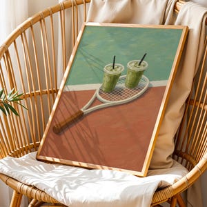以下が含まれることがあります： テニスラケットと2つの緑色の飲み物を描いた額入りのアートプリント。アートワークはテニスコートの背景と茶色の木製フレームです。プリントは籐の椅子に飾られています。
