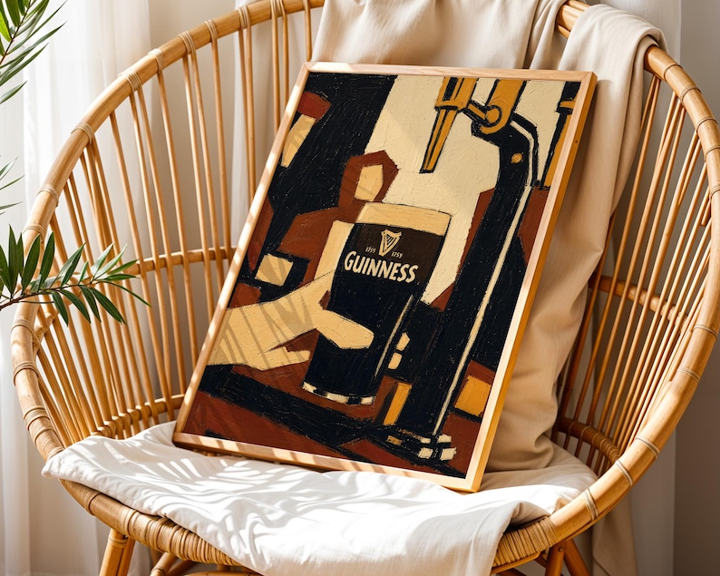 Op de afbeelding: Een ingelijste kunstafdruk met een Guinness-advertentie. Het kunstwerk toont een hand die een pint Guinness inschenkt, met het logo van het merk. Het kleurenpalet omvat zwart-, beige- en bruintinten, met een houten lijst.