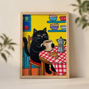 May include: A framed art print depicting a black cat enjoying coffee and a croissant at a table. The table has a red and white checked tablecloth. A coffee maker is also on the table. The background is yellow with blue and red cupboards and shelves.