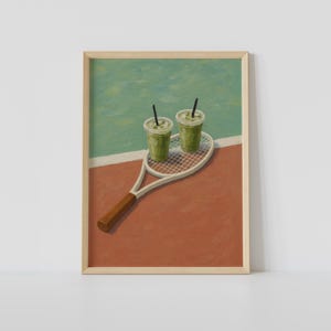 以下が含まれることがあります： テニスラケットに2つの緑色の飲み物が乗ったフレームプリント。ラケットは赤と緑の表面にあり、白い線で区切られています。飲み物には黒いストローが付いています。