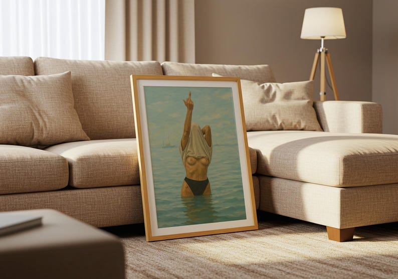 Puede incluir: Una impresi&oacute;n art&iacute;stica enmarcada que representa a una persona en el agua, levantando una camiseta. La obra de arte tiene una paleta de colores azul claro y beige, con un marco de madera. La imagen est&aacute; apoyada contra un sof&aacute; beige.