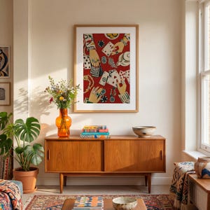 K&ouml;nnte beinhalten: Ein gerahmter Kunstdruck mit rotem Hintergrund, der H&auml;nde beim Kartenspielen, Pokermarker und Schmuck zeigt. Er h&auml;ngt &uuml;ber einem Holzschrank mit einer orangefarbenen Vase und einer Topfpflanze.