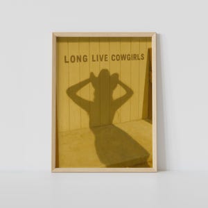 May include: Framed artwork featuring the text "LONG LIVE COWGIRLS" above a shadow of a person wearing a cowboy hat. The shadow is cast on a yellow wall, creating a warm, inviting aesthetic.