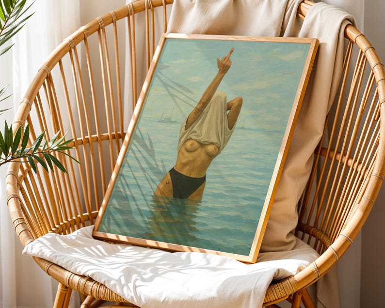 Puede incluir: Una impresi&oacute;n art&iacute;stica enmarcada representa a una persona en el agua, tirando de una camiseta sobre su cabeza. La obra de arte presenta una paleta de colores azul claro y turquesa, con un marco de madera. La persona lleva un traje de ba&ntilde;o negro. El arte se exhibe en una silla de mimbre.