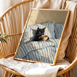 May include: A framed art print featuring a black cat holding a cup of coffee, resting on a bed with blue and white striped bedding. The artwork is in a wooden frame and is displayed on a wicker chair.