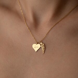 Puede incluir: Un collar dorado con un colgante en forma de coraz&oacute;n con la palabra "Love" grabada y un dije de ala. El collar se muestra en el pecho de una persona.