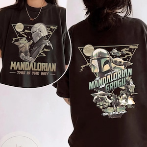 May include: Black t-shirt featuring a graphic of The Mandalorian and Grogu. The front design includes the text "MANDALORIAN - THIS IS THE WAY." The back design features the text "STAR WARS THE MANDALORIAN AND GROGU - THIS IS THE WAY."