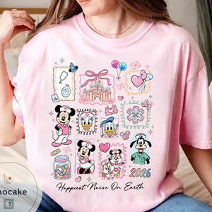 May include: Pink t-shirt with a colorful graphic featuring Disney characters in nurse attire. The design includes Mickey and Minnie Mouse, Donald Duck, and Goofy, along with medical symbols and the text "Happiest Nurse On Earth" and the year 2026.