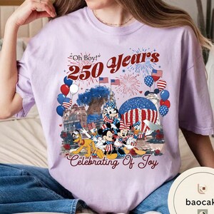 Puede incluir: Camiseta lila claro con un gr&aacute;fico que celebra 250 a&ntilde;os. El dise&ntilde;o incluye Mickey Mouse, Minnie Mouse, Donald Duck, Pluto, fuegos artificiales, globos y banderas americanas. El texto dice "Oh Boy!" y "Celebrating Of Joy."