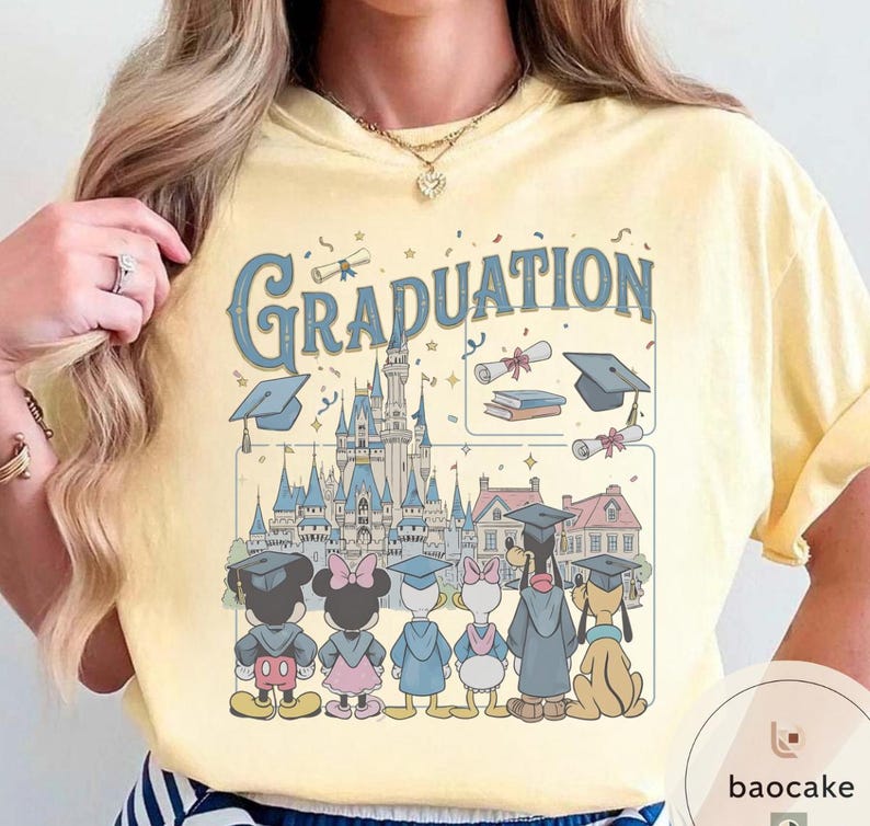 May include: Yellow t-shirt with a graphic featuring the word "Graduation" in blue script, a castle, and cartoon characters in graduation attire. The design includes Mickey and Minnie Mouse, Donald and Daisy Duck, and Pluto.